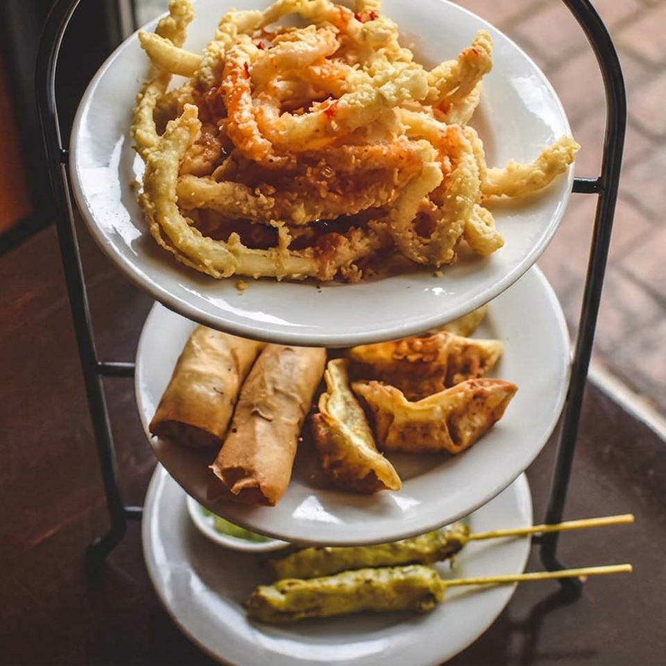 Three-tier serving stand displaying crispy tempura vegetables, spring rolls, dumplings, and skewered grilled appetizers.